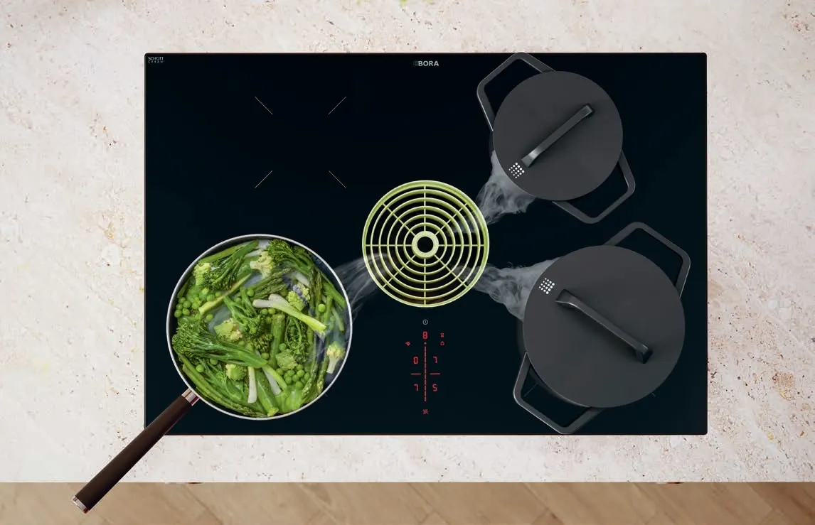 b2bogzgqpyrxtppn00d5 BORA Pure indukciona ploča sa zelenom ventilacionom mlaznicom i svežim povrćem u procesu kuvanja.